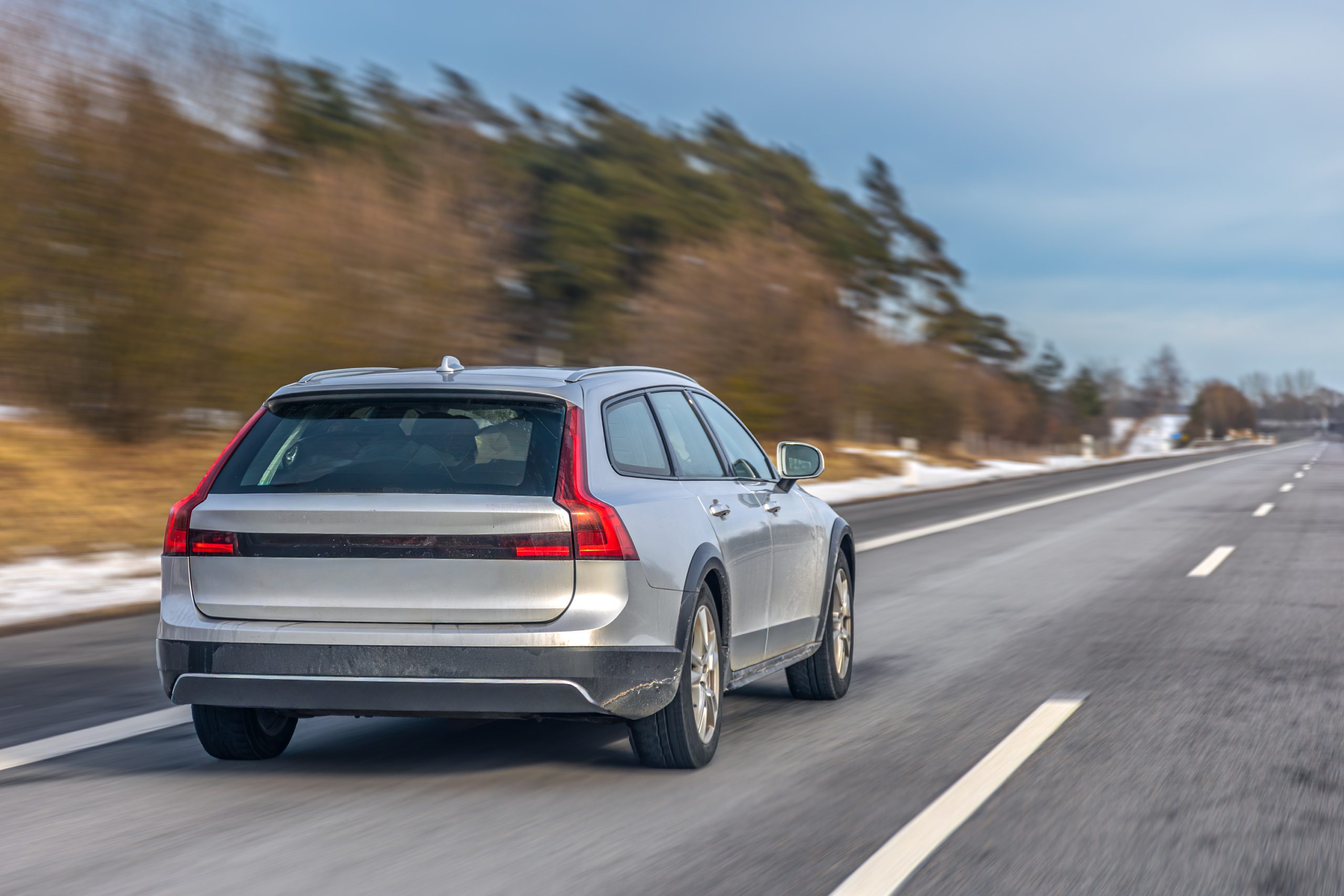 Silver station wagon traveling along a winter highway through rural landscape with motion blur effect. Concept of road travel, mobility and transportation.
