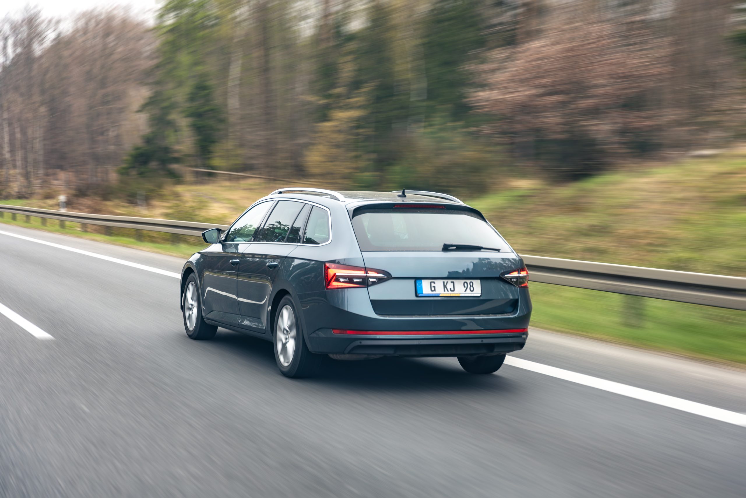 Dark station wagon driving on a highway beside a blurred forest roadside. Suitable for automotive mobility content, road travel articles, transport services, and driving safety campaigns.